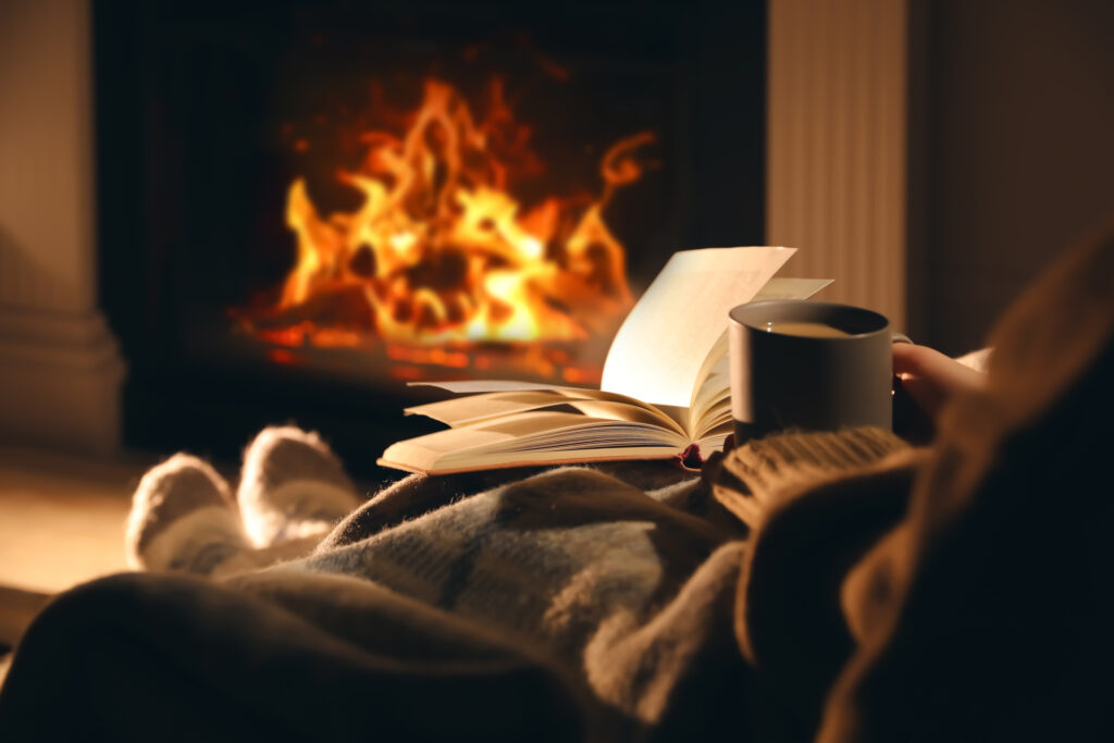Cozy winter scene with feet in warm socks near a CG wood fireplace, reading and drinking coffee