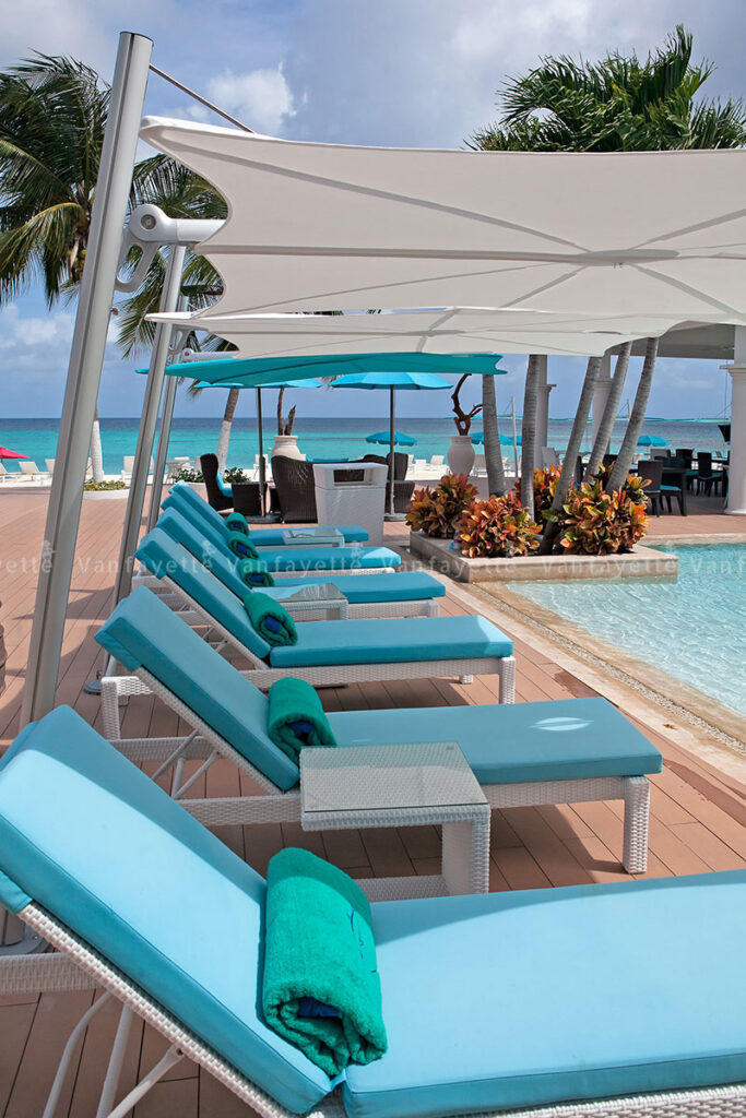Simplicity in Form, Serenity in Function – The Art of Outdoor Living White rattan sunbed with blue cushions and a designer white umbrella by the sea, showcasing CG Outdoor’s comfort and durability