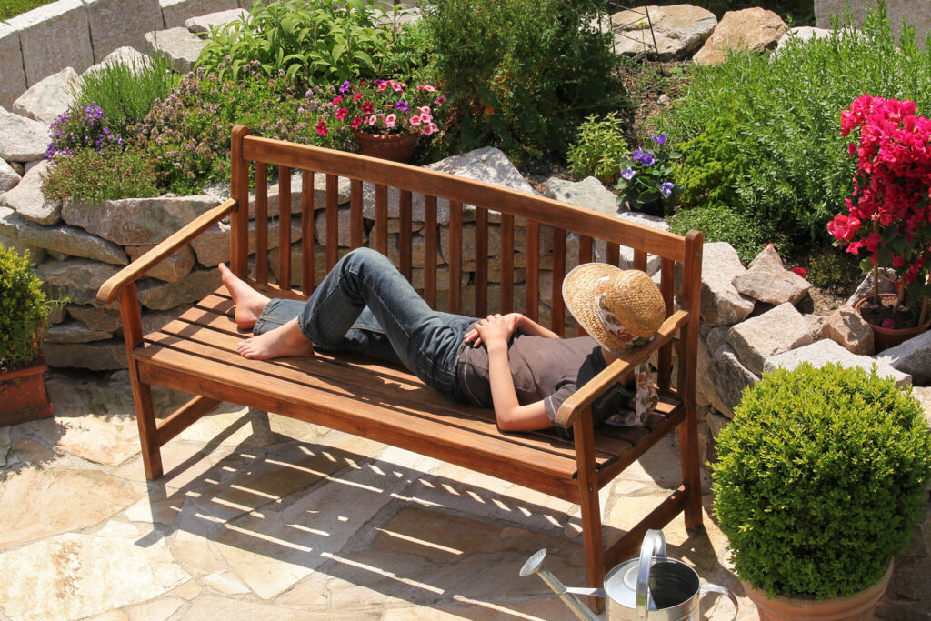 Teenager with sun hut is chilling on a teak bench.