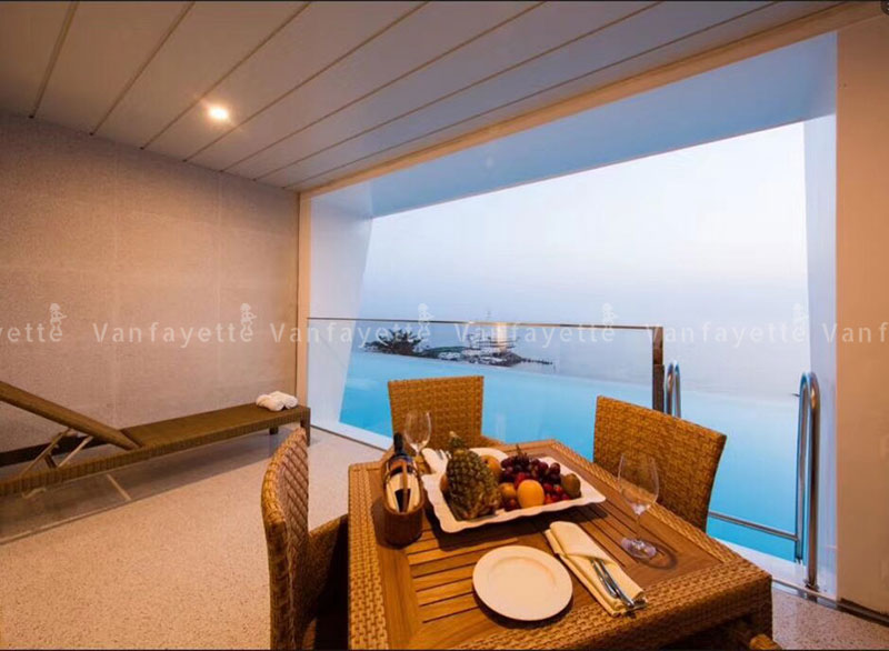 Indoors Out – Where Comfort Crosses the Threshold Hotel room balcony with floor-to-ceiling windows, furnished with CG’s rattan lounger and dining set featuring a teak table top