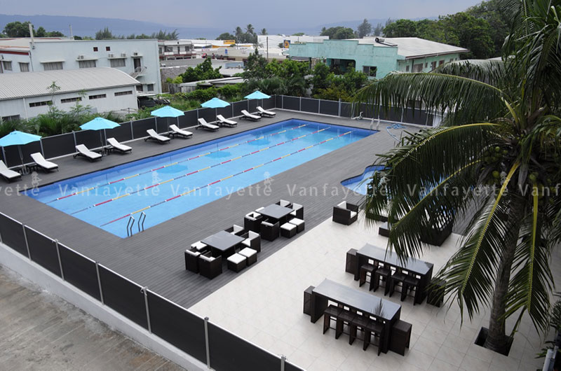 Classic brown rattan outdoor furniture with white cushions arranged around a hotel pool, including loungers, sofas, and bar sets
