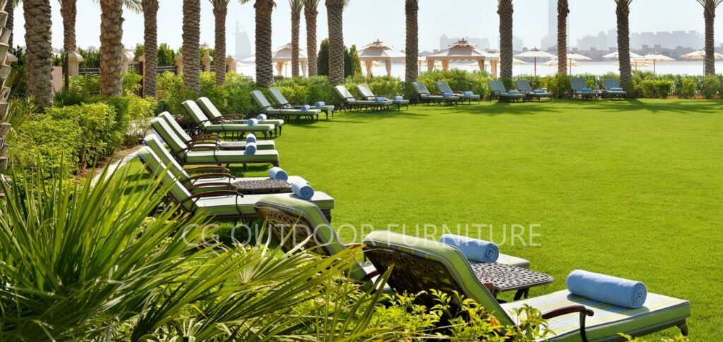 Dozens of aluminum pool deck loungers with thick cushions on a hotel lawn — tailored for comfort, scale, and durability