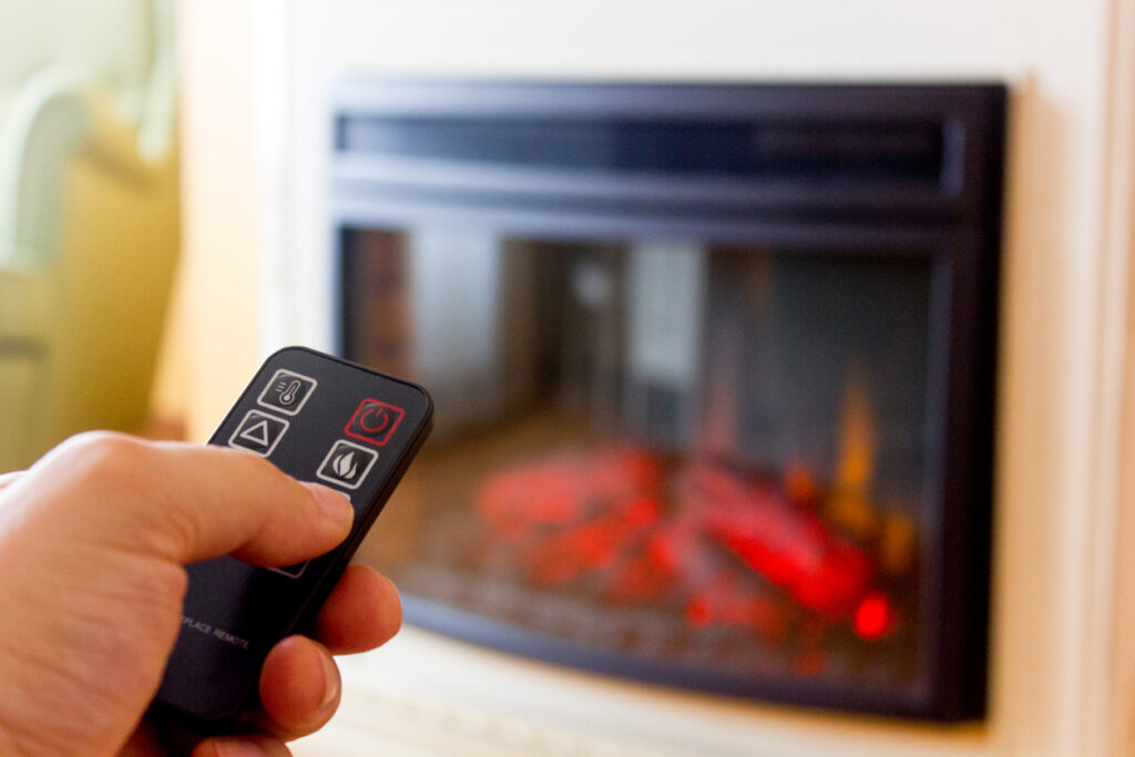 Turning On an Indoor Electric Fireplace with Remote Control hand holding a remote control turning on an indoor electric fireplace in a modern living room