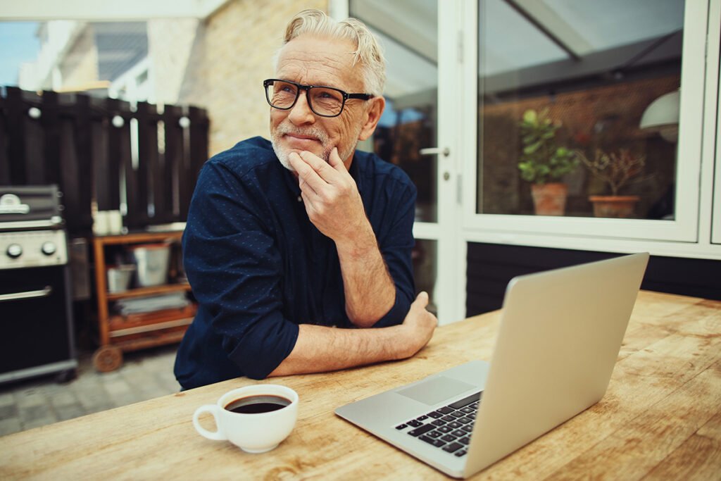 Man relaxing with coffee while working on a laptop in an outdoor patio setting
