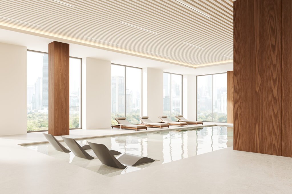 Luxury indoor pool with modern in-water lounge chairs and poolside loungers overlooking a city skyline.