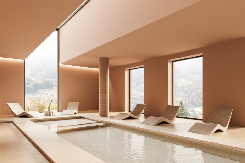 Modern indoor pool and spa with sculptural lounge chairs arranged in a spacious luxury wellness setting.