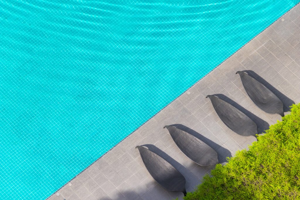 Top view of four sculptural outdoor poolside lounge chairs arranged beside a swimming pool with landscaped greenery.